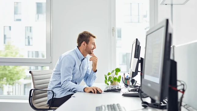 Ein Mann sitzt an einem Bürotisch und arbeitet an einem PC