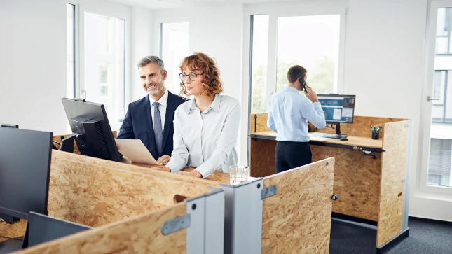 Drei Personen arbeiten in einem Büro an PCs